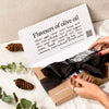 Black bow wrapping a box with a 'Flavours of olive oil' printed on top and pinecones on a light background