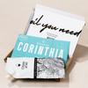 Delivery box containing 'Welcome to Corinthia' card and 'Citizens of Soil' olive oil pouch on a beige background