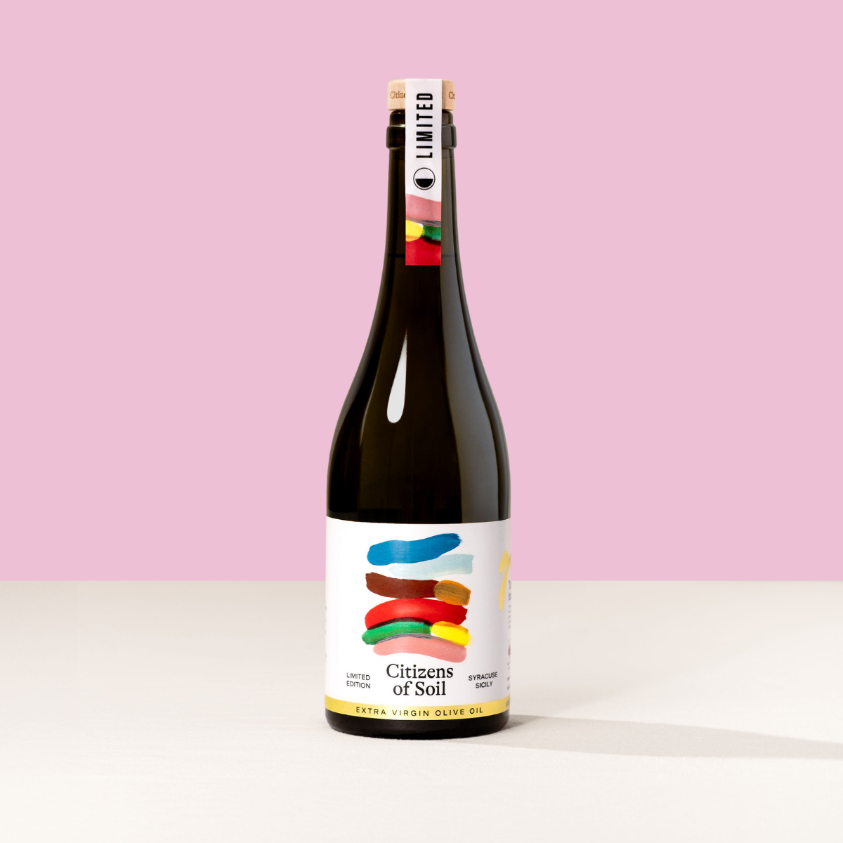 Bottle of Sicilian 'Citizens of Soil' olive oil with a colorful label on a pink background