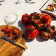 Assorted tomatoes on a wooden cutting board with a nonna knife, cookbook and olive oil container.