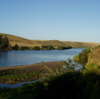 Landscape with a lake surrounded by greenery and hills under a clear blue sky.