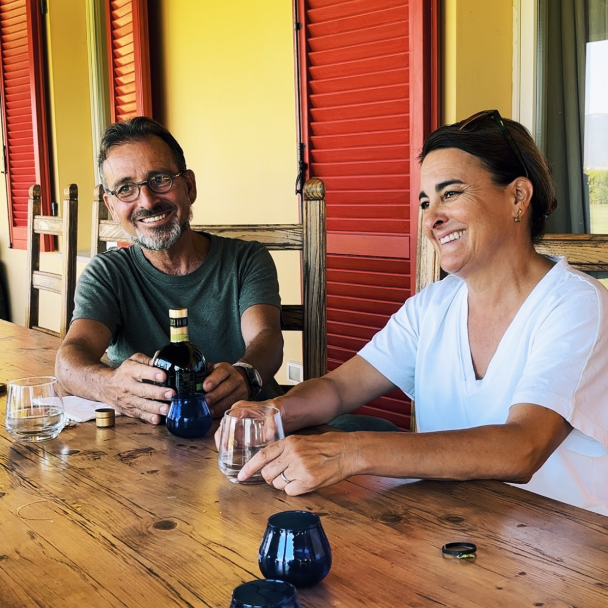 Man and woman smiling sitting at wooden table tasting olive oil