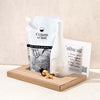 Olive Oil Club pouch with white Ceramic pourer in an open brown box on a white table