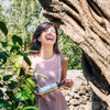 Woman laughing in olive grove holding an olive oil bottle
