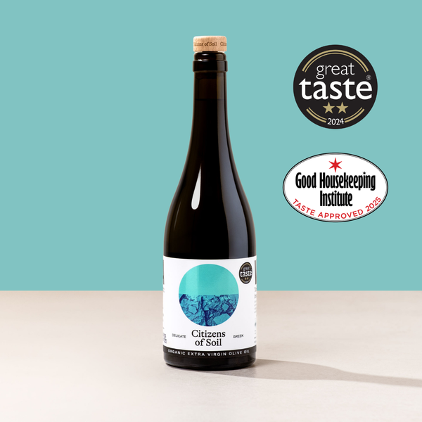 Bottle of greek extra virgin olive oil with 'Great Taste' and 'Good Housekeeping Institute' logos on a teal background
