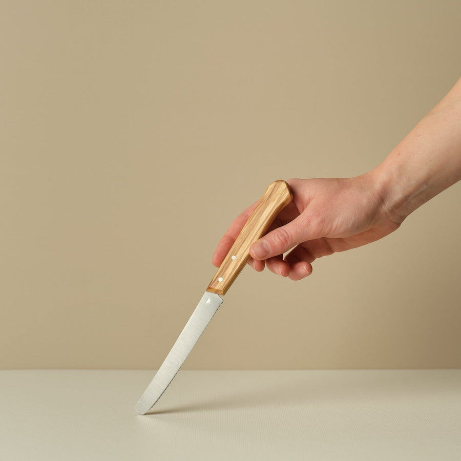Hand holding a knife with a wooden handle on a beige background