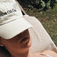 Woman laying in sun with white Olive Oil Club cap resting on face.