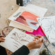 Person painting on a sketchbook with art supplies on a table