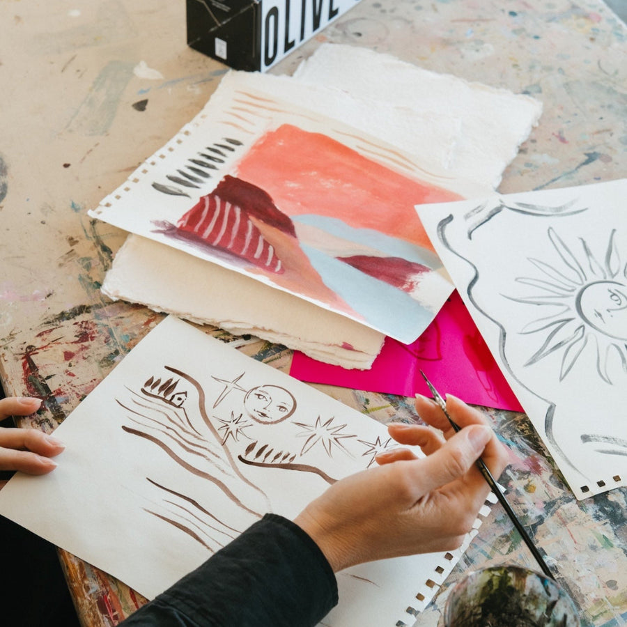 Person painting on a sketchbook with art supplies on a table